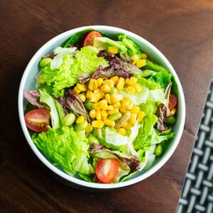 A vibrant salad with lettuce, cherry tomatoes, corn, and edamame in a white bowl.